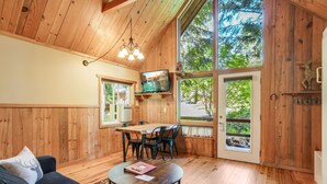 A cozy cabin interior with wooden walls, a dining area, a sofa, and a TV. - Beautiful Cabin With Partial Views of Mt. Adams (Trout Lake)