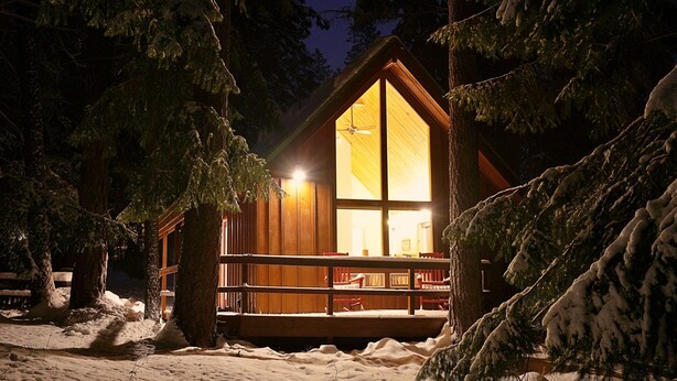 Een chalet met een groot raam, houten gevel en een terras.
