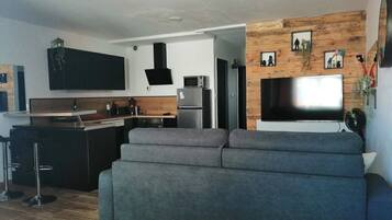 Una cocina moderna con horno empotrado, un televisor de pantalla plana grande montado en una pared de madera y un sofá gris en la sala.