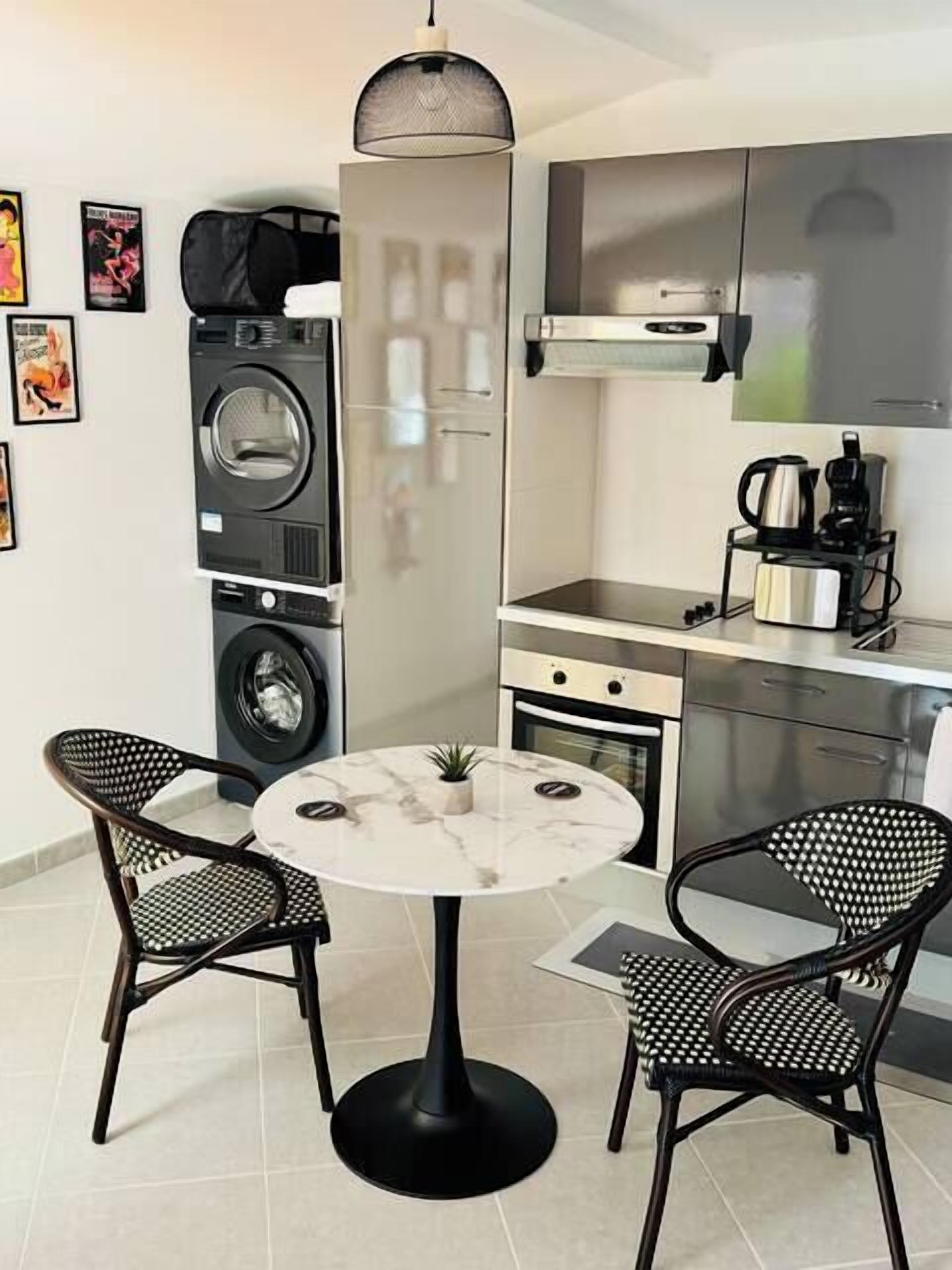 Una cucina compatta con lavatrice e asciugatrice integrate, un piccolo tavolo da pranzo con due sedie e una macchina da caffè sul ripiano.