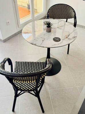 A round marble table with two black wicker chairs, a small potted plant, and a coaster. - Stylish City Pad – Walk to All (Bergerac)