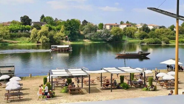 A lakeside park with picnic tables and umbrellas, boats on the water, and buildings in the background. - Stylish City Pad – Walk to All (Bergerac)