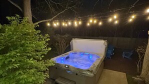 Un jacuzzi al aire libre con panel de control, rodeado por una terraza de concreto, bajo luces colgantes.