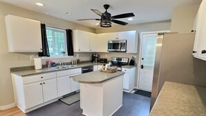 Una cocina moderna con armarios blancos, una isla central, un ventilador de techo y un microondas.