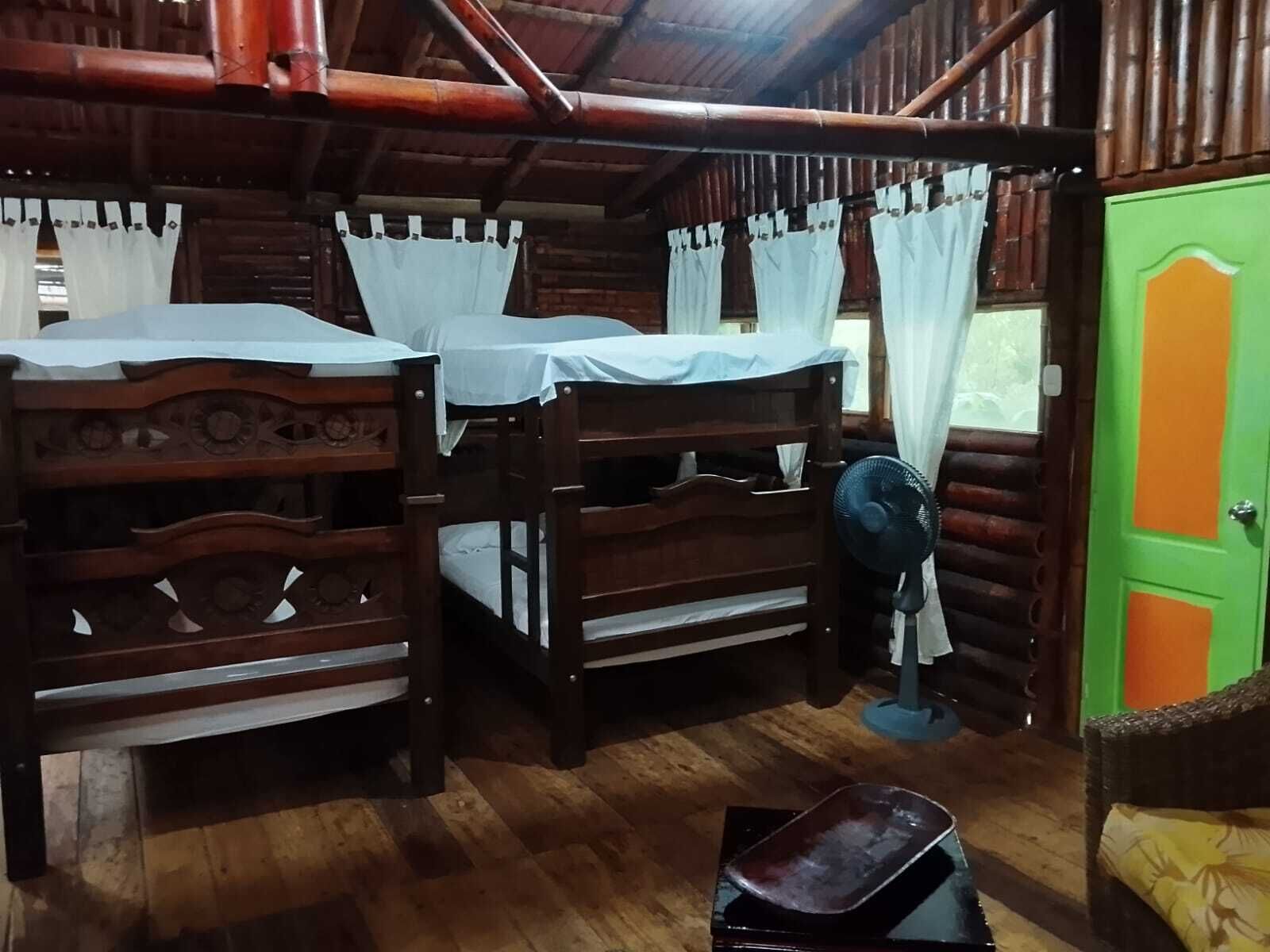 A rustic wooden room with two bunk beds, a fan, and a green door.