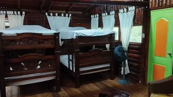 A rustic wooden room with two bunk beds, a fan, and a green door.
