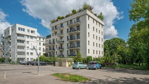 A multi-story residential building with balconies, a parking area, and surrounding greenery.