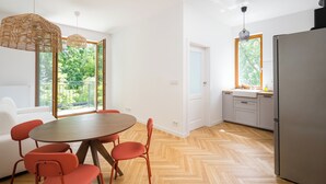 A modern kitchen with a large refrigerator, wooden herringbone flooring, and a dining area with a round table and red chairs.