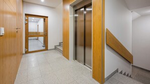 A modern hallway with a wooden door, a glass door, and a staircase leading to an elevator.
