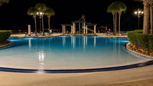 Ein Schwimmbecken bei Nacht mit Liegestühlen und Palmen.