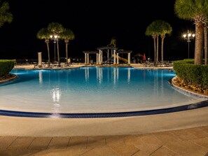 A nighttime swimming pool with lounge chairs and palm trees.