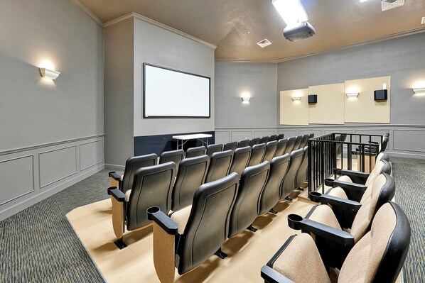A theater with rows of black and beige seats, a large screen, and wall-mounted lights.