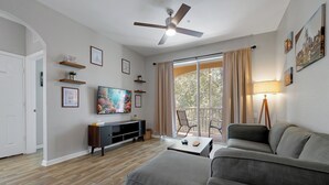 Ein modernes Wohnzimmer mit grauem Sofa, Fernseher und Deckenventilator.