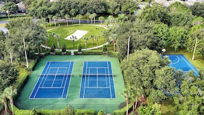Eine Vogelperspektive auf einen Tennisplatzkomplex, umgeben von üppiger Vegetation und Wohngebäuden.