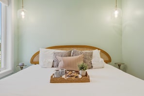 A neatly made bed with a tray of breakfast items, two bedside tables, and a window with a view.