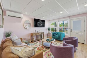 Una sala de estar con un sofá, sillones, una mesa de centro, un televisor y una puerta que da a un balcón.