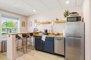 A kitchen with a refrigerator, microwave, coffee maker, and bar stools.