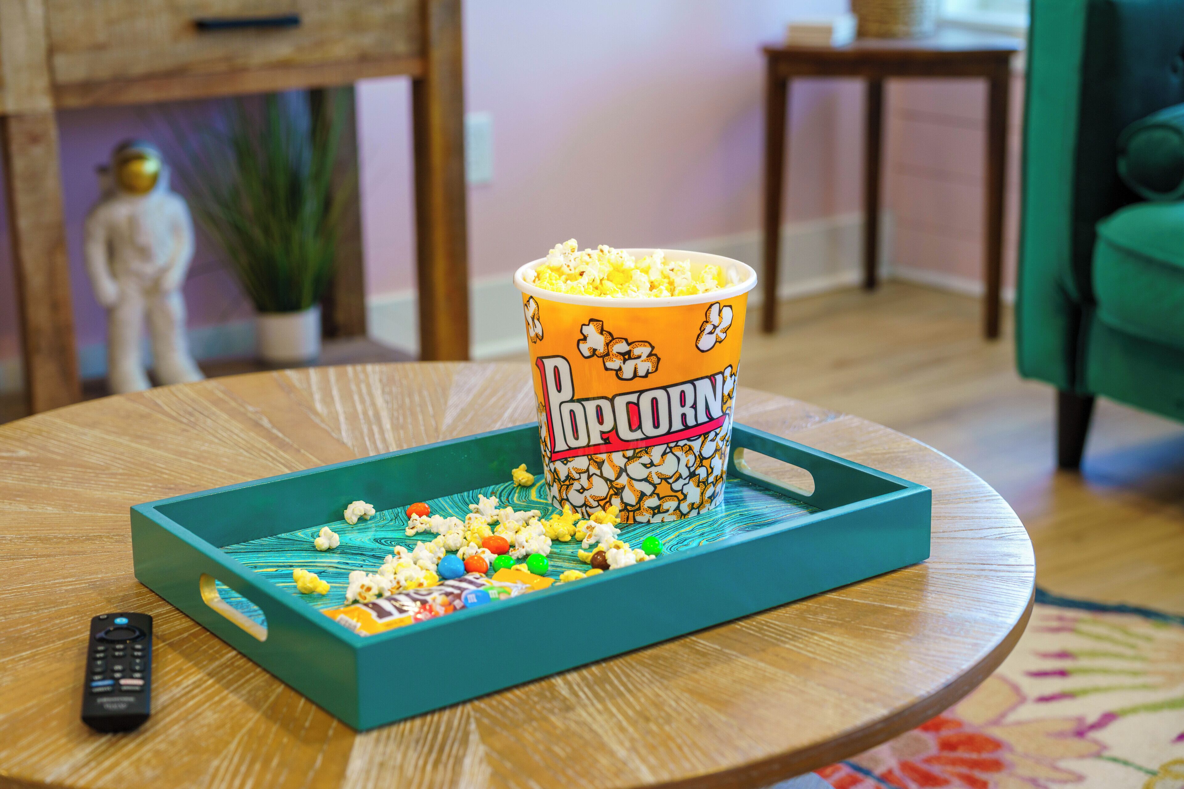 A popcorn container on a tray with various candies on a wooden table.