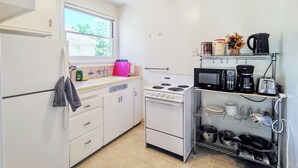 Une cuisine de taille réduite avec des meubles blancs, une cuisinière, un four à micro-ondes et une machine à café.