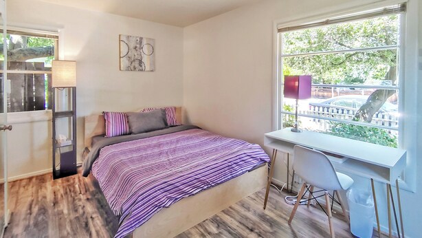 Une chambre à coucher avec un lit, un bureau, une chaise, une fenêtre et une porte.