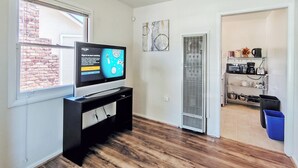 Un salon moderne doté d’un téléviseur à écran plat, d’un plancher en bois, d’un coin cuisine équipé d’appareils électroménagers et d’un mur en briques apparentes.