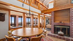 A spacious room with a large wooden dining table surrounded by chairs, a fireplace, and large windows offering views of the outdoors. - Cozy Getaway Ranch House and Estate by Yosemite (Jamestown)