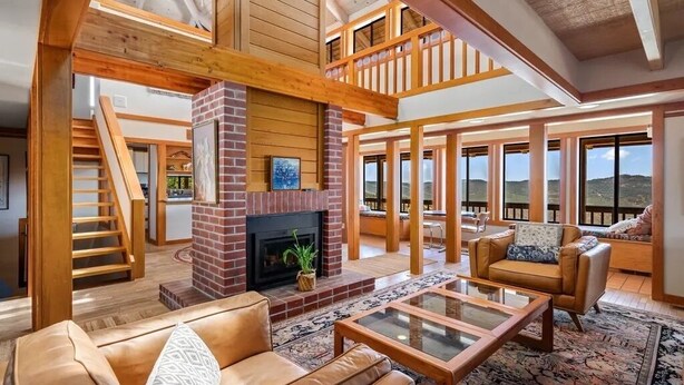 A spacious living area with a fireplace, a staircase, and large windows offering views of the outdoors. - Cozy Getaway Ranch House and Estate by Yosemite (Jamestown)