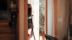 Une porte qui mène à une pièce dont l’intérieur est en bois, où l’on trouve un porte-manteau et une fenêtre donnant sur des arbres.