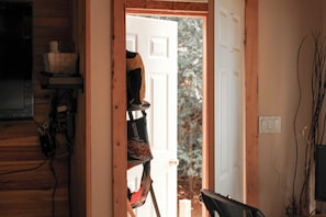 A doorway leading to a room with a wooden interior, a coat rack, and a visible window with a view of trees.