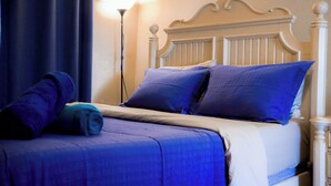 Un lit bien fait, avec une literie bleue, une tête de lit blanche et une serviette enroulée posée sur le côté.