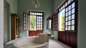 Une salle de bain avec une baignoire sur pieds, un meuble en bois et une grande fenêtre donnant sur un paysage verdoyant.