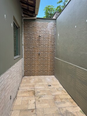 Enjoy a refreshing outdoor shower in a, enclosed space with a geometric-patterned wall and a window for natural ventilation.