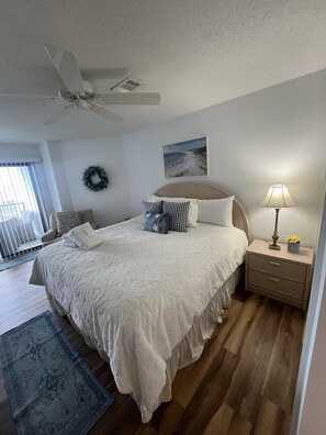 A bedroom with a bed, a nightstand, a lamp, a ceiling fan, a picture on the wall, and a view of the outside. - Stunning Oceanfront 2BR Villa with Panoramic Atlantic Views (Hilton Head Island)