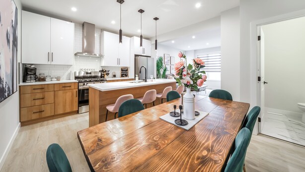 A modern kitchen with white cabinets, a wooden dining table, and teal chairs. - ExoticLUSHquietRetreatKingBed|WIFI|Parking|WEM (Edmonton)