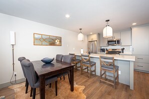 Uma cozinha moderna com uma ilha central, eletrodomésticos de aço inoxidável e uma área de jantar com mesa e cadeiras de madeira.
