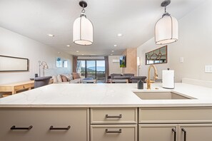 A modern kitchen with a large island, pendant lights, and a view of the outdoors.