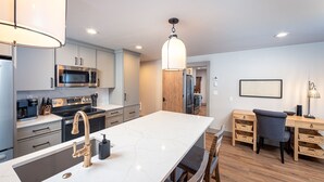 Une cuisine moderne dotée d’un îlot central, d’appareils électroménagers en acier inoxydable et d’un coin repas en bois.
