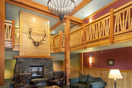 A spacious lobby with a stone fireplace, leather sofas, and a wooden ceiling with a deer antler decoration.