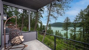 Ein Balkon mit einer Hängematte, einem Betonboden und Blick auf einen See, der von Bäumen und Hügeln umgeben ist.