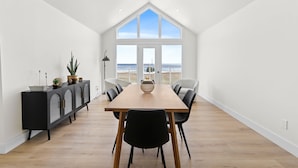 A modern dining room with a wooden table, black chairs, and a black cabinet with glass doors. - Foley’s Harbour House (Alberton)