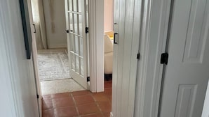 Ein Flur mit weißen Türen, Fliesenboden und einem sichtbaren Zimmer mit einem Bett.
