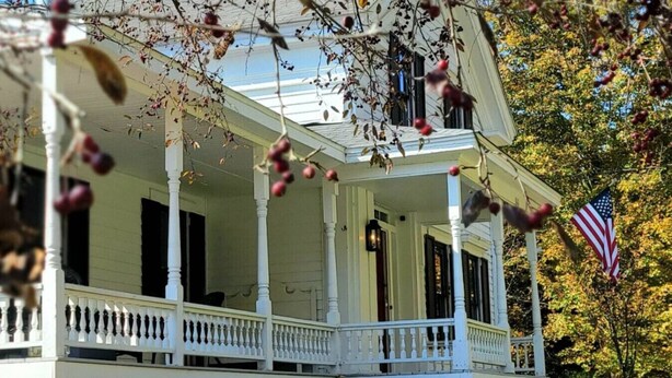 Ein weißes Haus im Kolonialstil mit Veranda, einer Flagge und Herbstlaub.