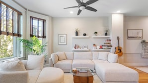 Un salon moderne avec un canapé d’angle, une table basse en verre et un ventilateur de plafond.