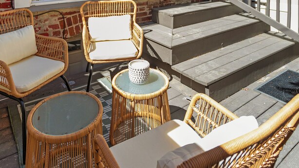 Une terrasse dotée de meubles en osier, d’une table en verre et d’une rambarde blanche.