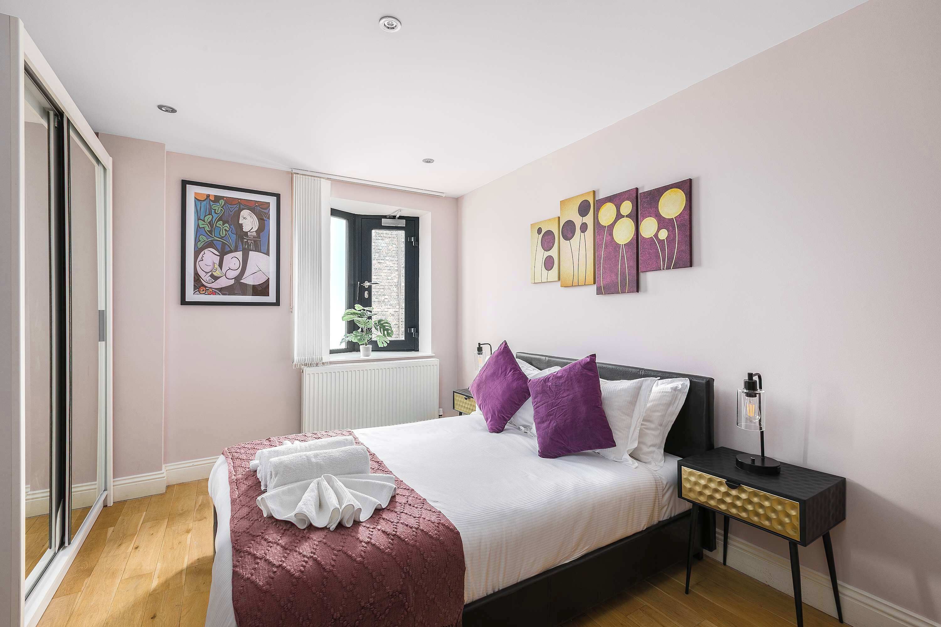 Un dormitorio con cama, una mesita de noche, una ventana y obras de arte en las paredes.