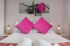 A bed with white bedding and two pink pillows, a bedside table with a lamp, and a wall with a rose artwork. - Modern Hoxton 2BR 2Bath Apartment with Balcony Sleeps 6 (Greater London)