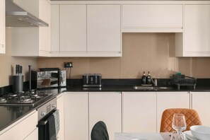 A modern kitchen with white cabinets, a black countertop, a stove, a toaster, and a dining area with a chair and table.