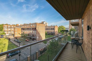 A balcony with a view of a multi-story residential building, a street with cars, and a clear sky. - Modern Hoxton 2BR 2Bath Apartment with Balcony Sleeps 6 (Greater London)