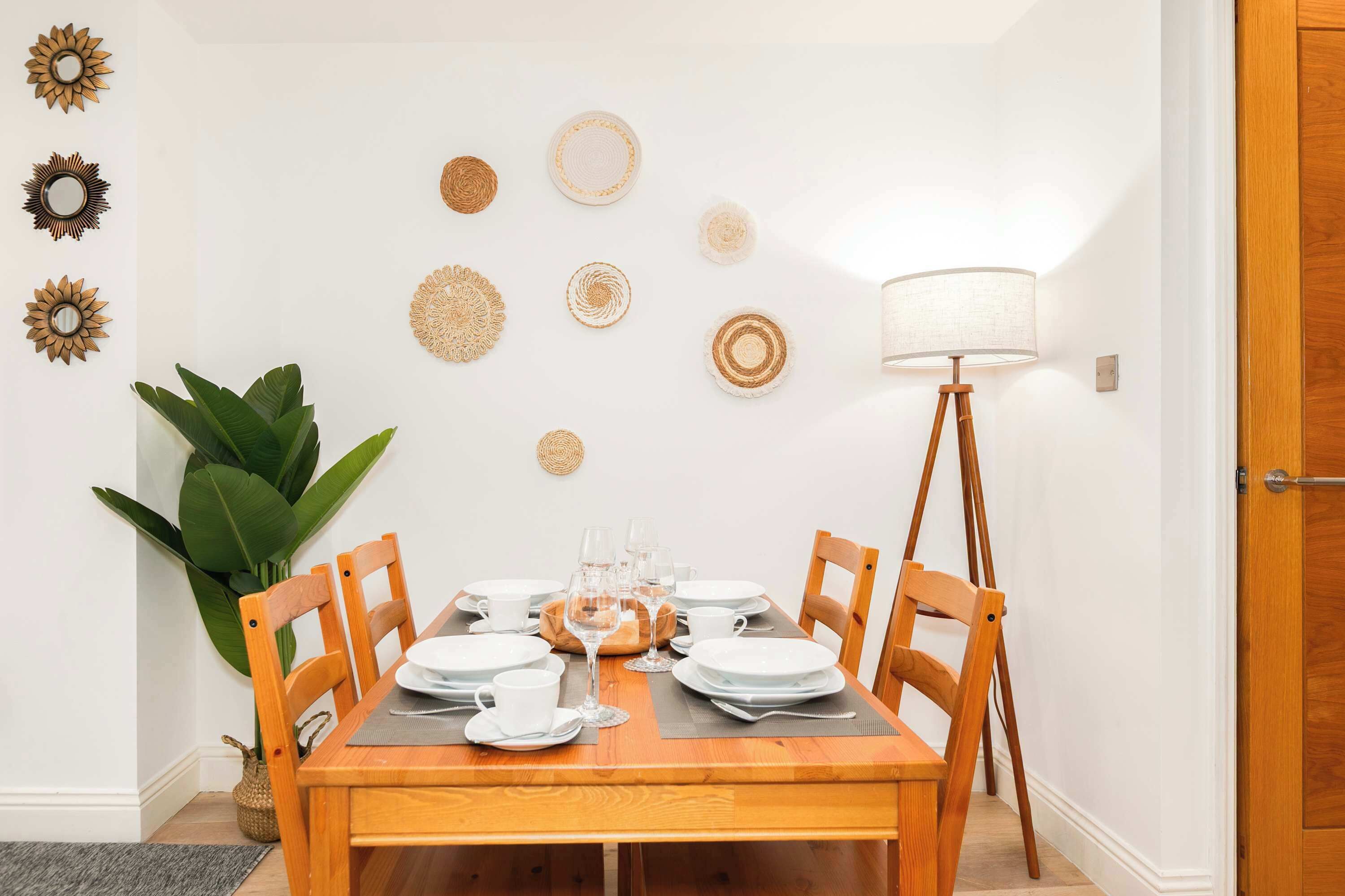 A dining area with a wooden table set for four, surrounded by chairs, with decorative wall art and a floor lamp.