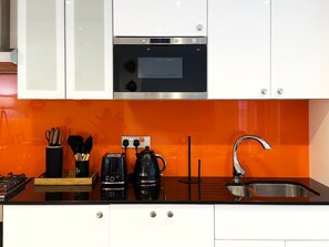 A kitchen with white cabinets, a black countertop, a stainless steel sink, and a black electric kettle. - Angel 2 BR, 2 Bath Duplex with Balcony Sleeps 5 (Greater London)